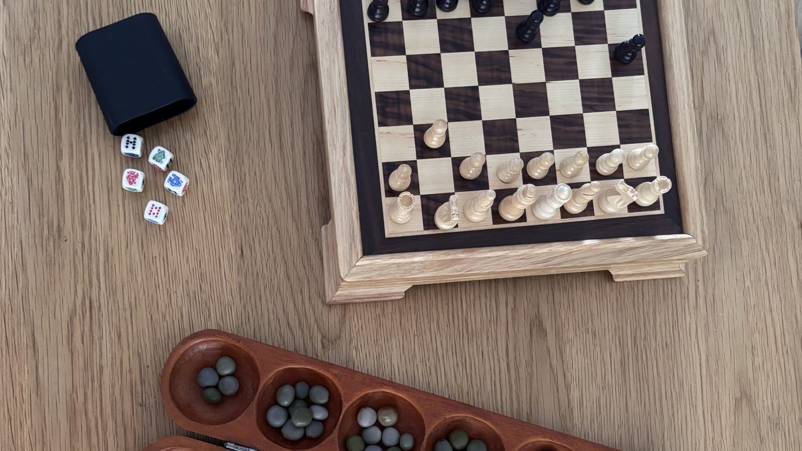 Chess board, dice, and wooden mancala board arranged on a table.
